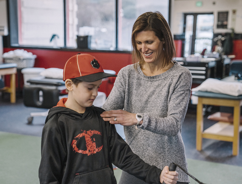 Physical therapist Talia Eubanks performing shoulder rehabilitation on a young boy wearing a red hat